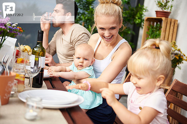 Ehepaar mit Baby- und Kleinkind-Töchtern beim Familienessen auf dem Terrassentisch