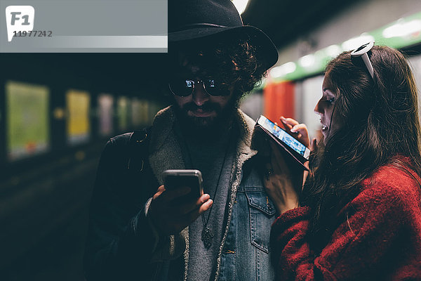 Junges Paar sitzt auf dem U-Bahnsteig und schaut auf Smartphones