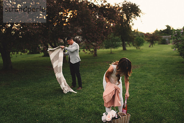 Junges Paar bereitet in der Abenddämmerung im Park eine Picknickdecke und rosa Champagner