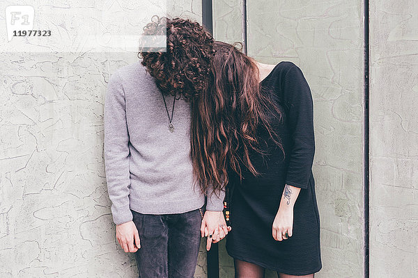 Junges Paar im Freien  an der Wand stehend  Hände haltend  Haare im Gesicht