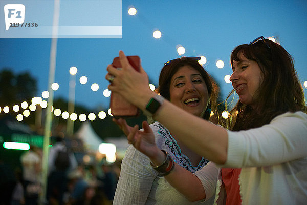 Zwei reife Freundinnen beim Smartphone-Selfie auf dem Nachtmarkt-Festival im Park  London  Großbritannien