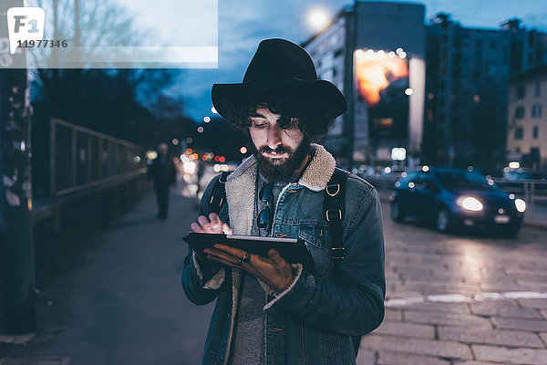 Junger Mann steht in der Abenddämmerung auf der Straße und benutzt ein digitales Tablett
