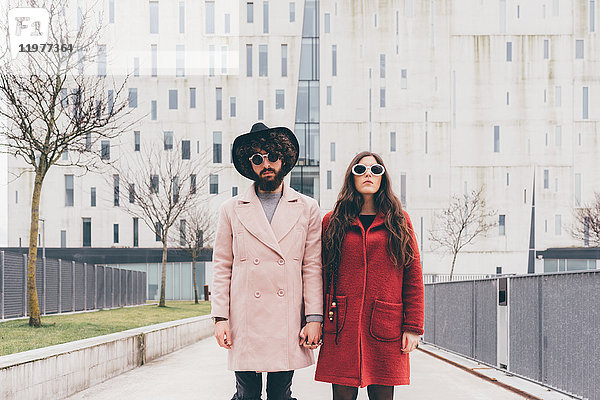 Porträt eines jungen Paares in städtischer Umgebung  Sonnenbrille tragend  Händchen haltend
