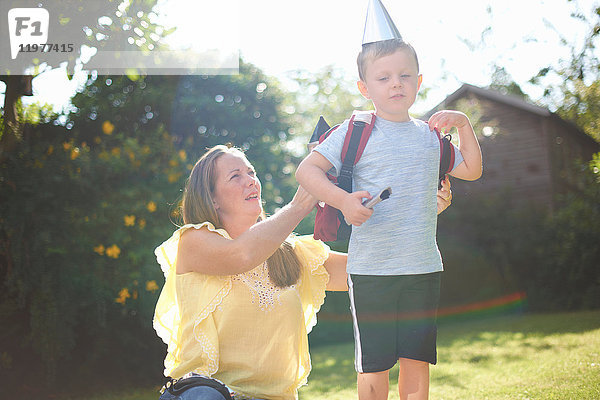 Reife Frau legt ihrem Sohn im Garten einen Raketenkostüm-Rucksack an