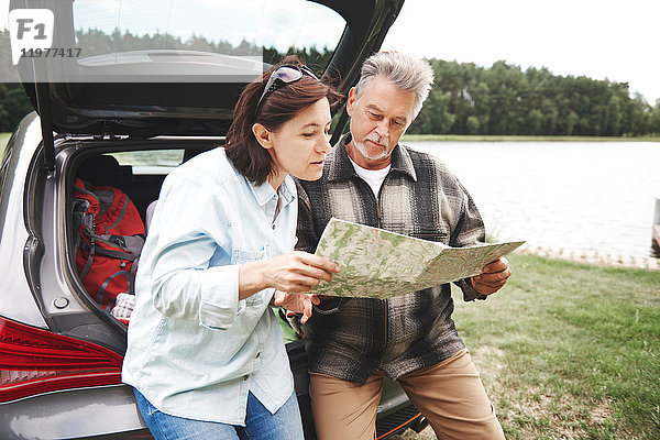 Älteres Ehepaar in ländlicher Umgebung  steht neben dem Auto und schaut auf die Karte