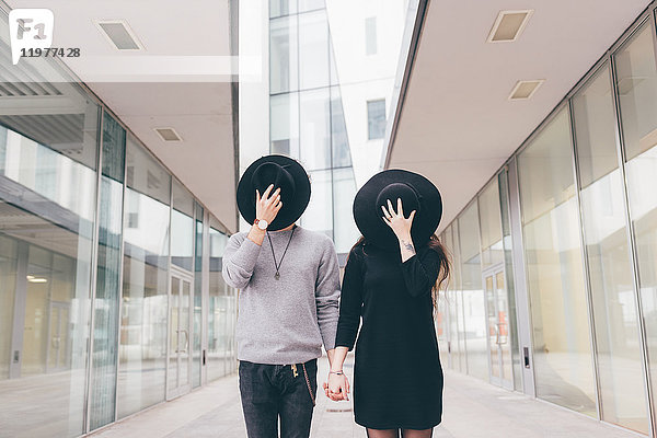 Porträt eines jungen Paares in städtischer Umgebung  Hände haltend  Gesichter mit Hüten bedeckt