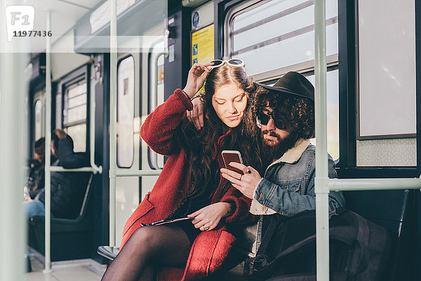 Junges Paar sitzt in der U-Bahn und schaut auf ein Smartphone