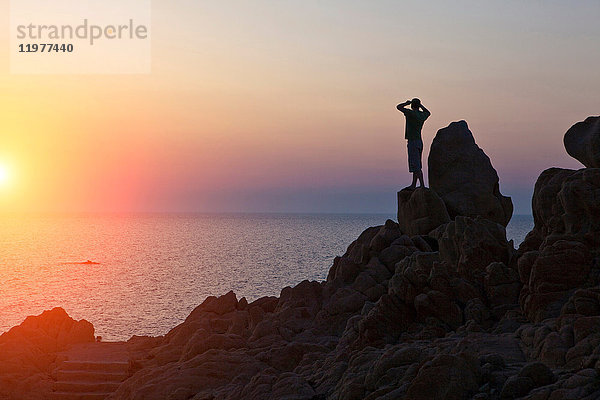 Silhouette eines Mannes auf Felsen  der den Sonnenuntergang über dem Meer betrachtet  Olbia  Sardinien  Italien