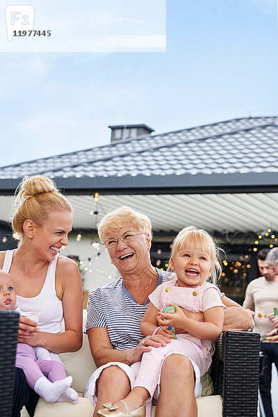 Frauen der dritten Generation mit Kindern auf dem Schoß beim Familienessen auf der Terrasse
