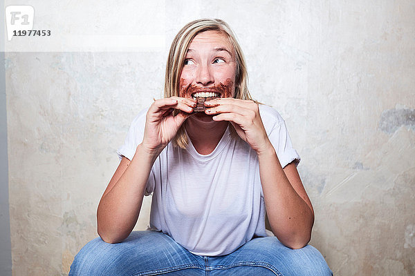 Porträt einer Frau  die eine Tafel Schokolade isst  Schokolade um den Mund