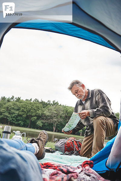 Reife Frau entspannt sich im Zelt  Mann vor dem Zelt  schaut auf die Karte