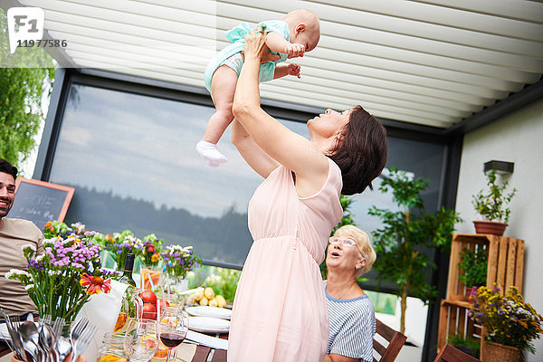 Reife Frau hebt Baby-Enkelin beim Familienessen auf der Terrasse hoch