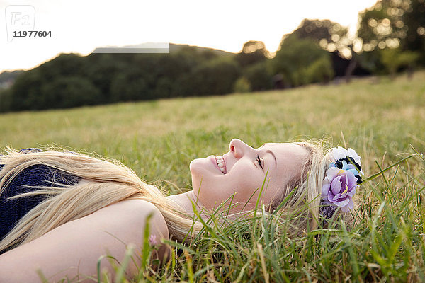 Frau mit Blumen im Haar lächelnd auf Gras liegend