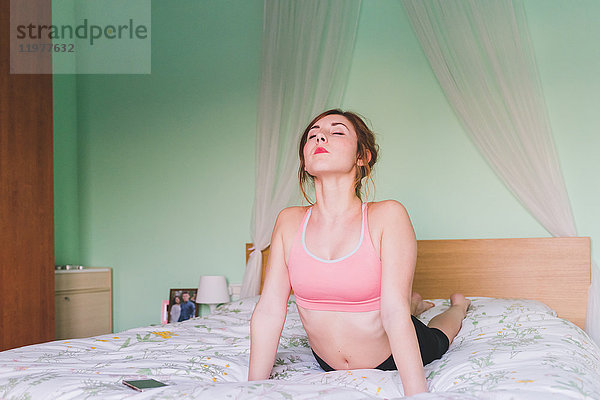 Junge Frau  die Yoga praktiziert  liegt auf der Vorderseite und beugt sich auf dem Bett zurück
