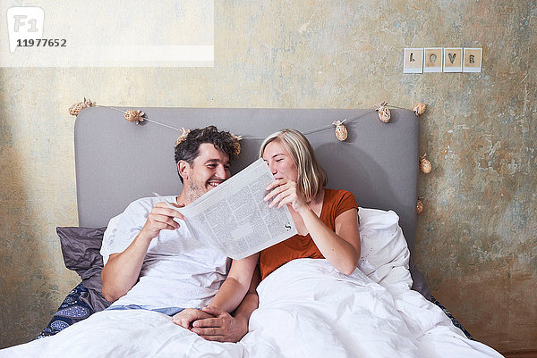 Paar im Bett  Händchen haltend  Zeitung austauschen