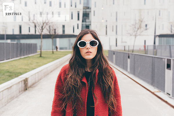 Porträt einer jungen Frau mit Sonnenbrille  stehend in städtischer Umgebung