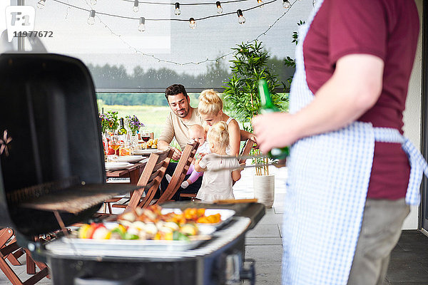 Mann grillt beim Familienessen auf der Terrasse