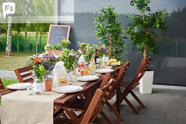 Tisch mit Blumenarrangements und Tellern für das Mittagessen auf der Terrasse