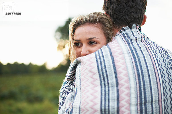 Junges Paar umarmt sich in eine Decke gehüllt im Feld
