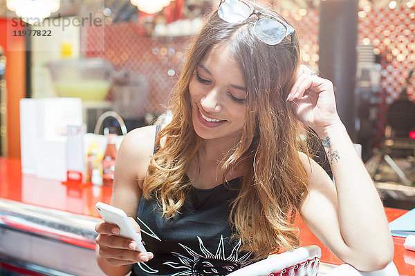 Junge Frau sitzt im Cafe  schaut auf Smartphone und lächelt