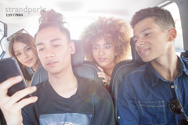 Vier Freunde im Taxi  die sich ein Smartphone anschauen