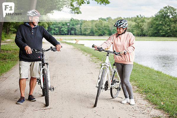 Ein erwachsenes Paar  das mit Fahrrädern den ländlichen Weg entlang fährt und lächelt