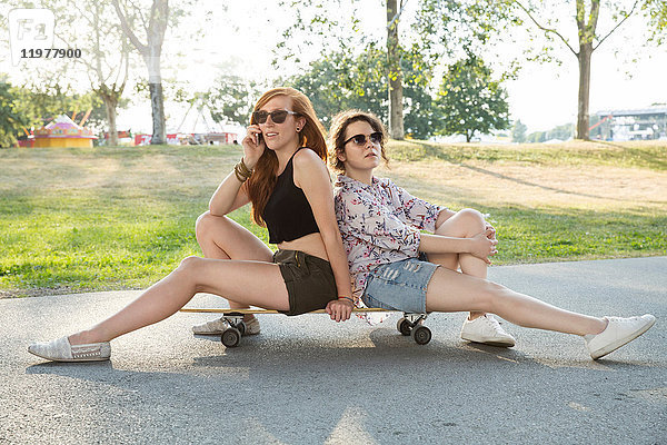 Porträt von zwei jungen Frauen im Freien  die auf einem Skateboard sitzen