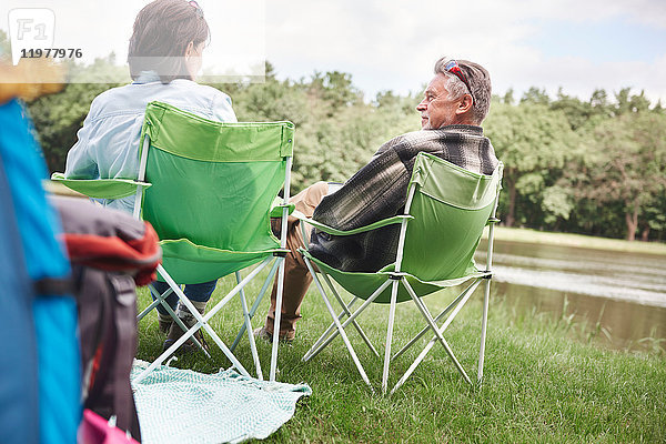 Älteres Paar sitzt in Campingsesseln am See  Rückansicht