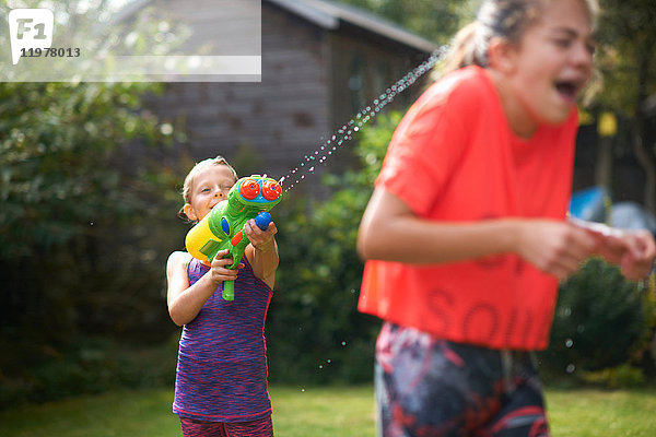 Junge bespritzt seine jugendlichen Schwestern mit Wasserpistole im Garten