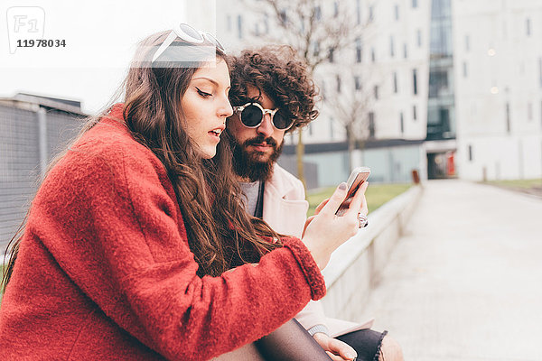 Junges Paar sitzt im Freien und schaut auf ein Smartphone