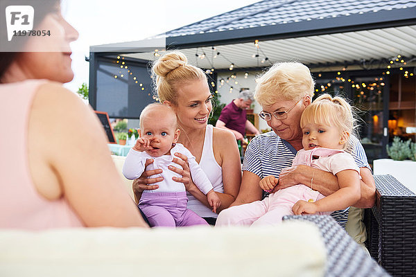 Ältere und junge Frauen mit weiblichem Kleinkind und Baby Girl auf dem Schoß beim Familienessen auf der Terrasse