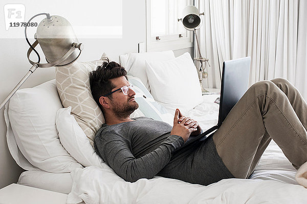 Mittelgroßer erwachsener Mann im Bett liegend  mit Laptop