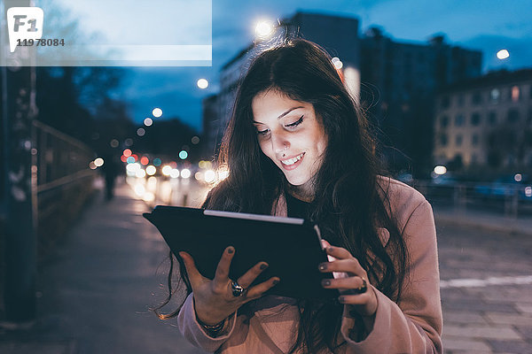 Junge Frau  im Freien  nachts  Blick auf digitales Tablett  Gesicht beleuchtet