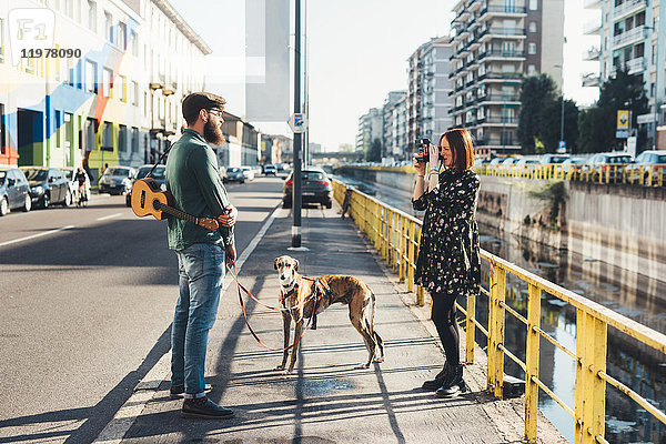 Junge Frau fotografiert Freund und Hund am Kanal mit Sofortbildkamera