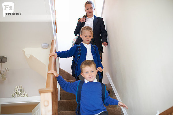 Teenager-Schülerin mit Schwester und Bruder in Uniform zieht die Treppe hinunter