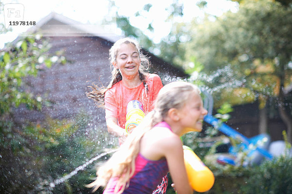 Teenager-Mädchen und ihre Schwester bespritzen sich gegenseitig im Garten mit Wasserpistolen