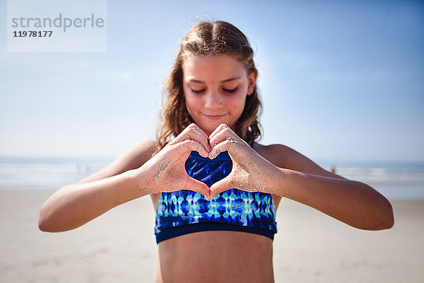 Mädchen macht Herzform mit Händen am Strand