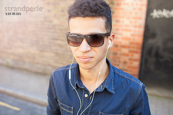 Porträt eines jungen Mannes im Freien  der eine Sonnenbrille und Kopfhörer trägt