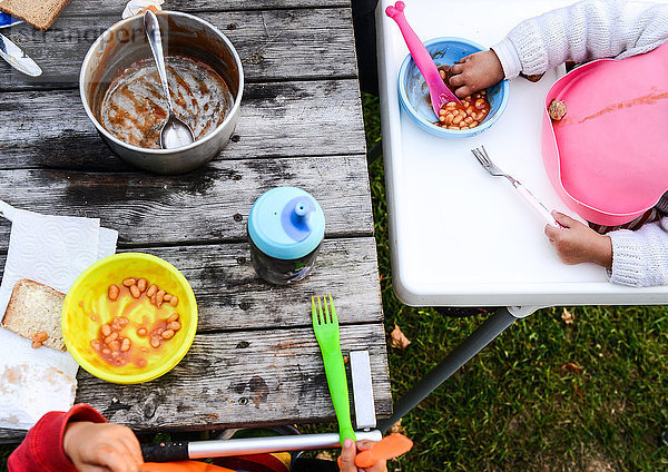 Geschnittene Draufsicht auf zwei Kleinkinder  die auf dem Campingplatz gebackene Bohnen essen