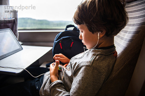 Kleiner Junge reist im Zug  benutzt ein digitales Tablet und trägt Kopfhörer