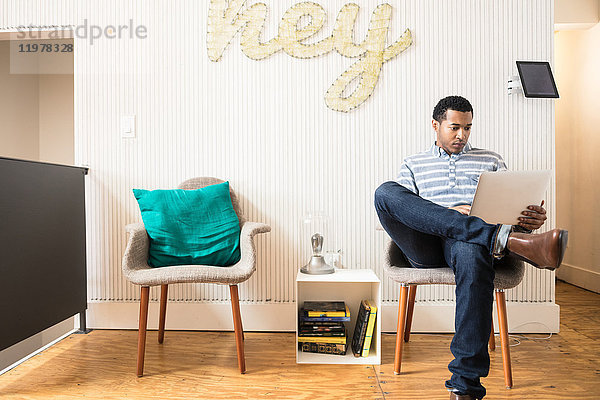 Cooler junger Geschäftsmann sitzt mit Laptop im kreativen Bürosessel