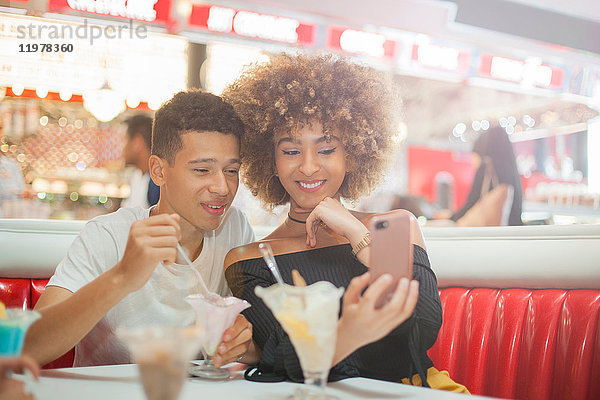 Junges Paar sitzt im Diner  schaut auf Smartphone  lacht