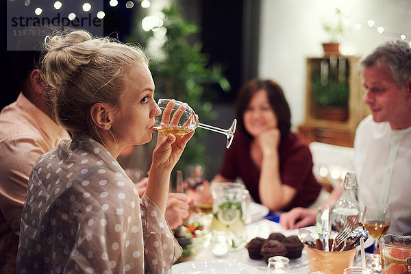 Gruppe von Personen  die am Tisch sitzen  eine Mahlzeit genießen  junge Frau trinkt aus einem Weinglas