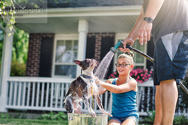 Vater und Tochter waschen Hund mit Schlauch