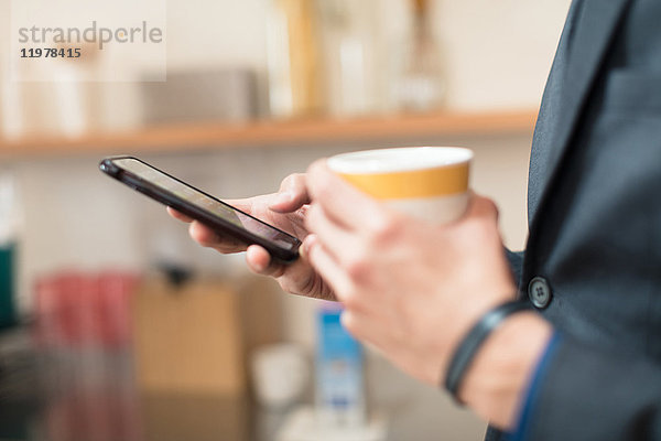 Hände eines Geschäftsmannes mit Kaffeetasse und Smartphone