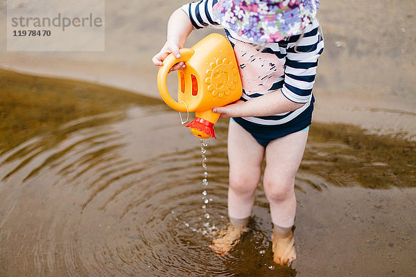 Mädchen steht knöcheltief im See und giesst Wasser aus einer Spielzeuggiesskanne  Huntsville  Kanada