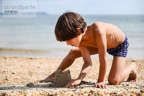 Junge macht Sandburg am Strand