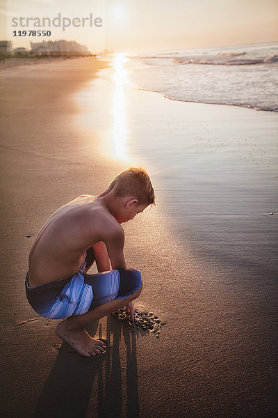 Junge zeichnet Sand am Strand ein
