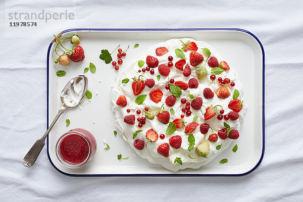 Pavlova mit roten Johannisbeeren  Erdbeeren und frischer Minze auf Serviertablett