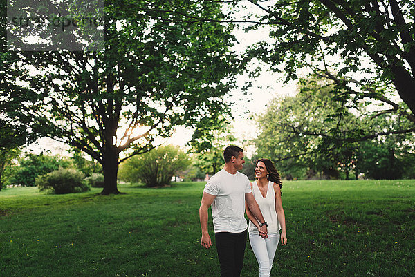 Romantisches junges Paar schlendert im Park und hält Händchen